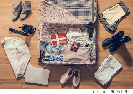 Woman's clothes, laptop, camera, russian passport and flag of Denmark lying on the parquet floor near and in the open suitcase. Travel concept Woman's clothes, laptop, camera, russian passport and flag of Denmark lying on the parquet floor near and in the open suitcase. Travel concept 90953496