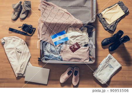 Woman's clothes, laptop, camera, russian passport and flag of Argentina  lying on the parquet floor near and in the open suitcase. Travel concept 90953506