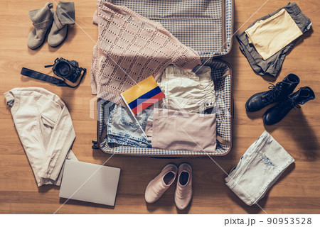 Woman's clothes, laptop, camera and flag of Colombia lying on the parquet floor near and in the open suitcase. Travel concept Woman's clothes, laptop, camera and flag of Colombia lying on the parquet floor near and in the open suitcase. Travel concept 90953528