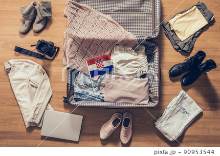 Woman's clothes, laptop, camera and flag of Croatia lying on the parquet floor near and in the open suitcase. Travel concept Woman's clothes, laptop, camera and flag of Croatia lying on the parquet floor near and in the open suitcase. Travel concept 90953544