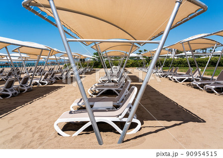 A rows of sunbeds at a deserted sandy beach in turkish resort. Sun loungers waiting for tourists in a hotel 90954515