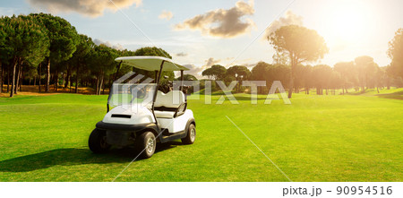 Golf cart in fairway of golf course with green grass field with cloudy sky and trees at sunset Golf cart in fairway of golf course with green grass field with cloudy sky and trees at sunset 90954516