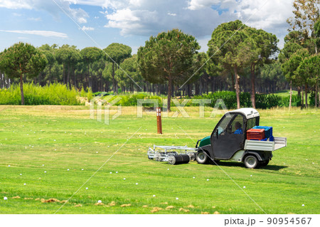 Golf course and golf cart collecting golf balls. Ballpicker on driving range of golf club Golf course and golf cart collecting golf balls. Ballpicker on driving range of golf club 90954567