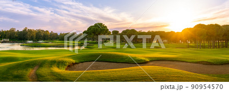 Golf course at sunset with beautiful sky and sand trap. Scenic panoramic view of golf fairway with bunker. Golf field with pines Golf course at sunset with beautiful sky and sand trap. Scenic panoramic view of golf fairway with bunker. Golf field with pines 90954570