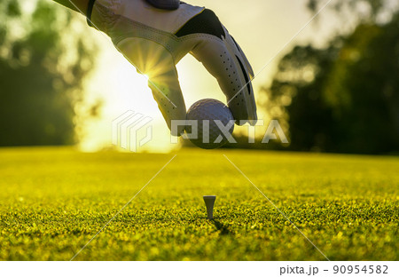 Closeup of golfer wearing glove placing golf ball on a tee at golf course 90954582