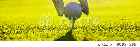 Closeup of golfer wearing glove placing golf ball on a tee at golf course Closeup of golfer wearing glove placing golf ball on a tee at golf course 90954599