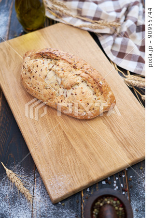 Fresh bread loaf on wooden cutting board at kitchen table Fresh bread loaf on wooden cutting board at kitchen table 90955744