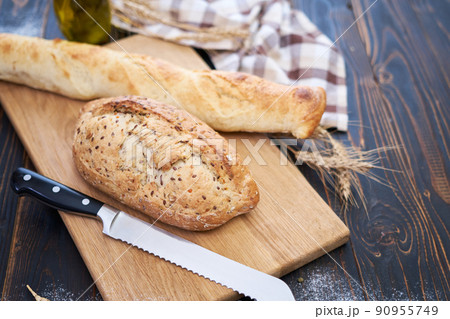 Fresh bread loaf and baguette on wooden cutting board at kitchen table Fresh bread loaf and baguette on wooden cutting board at kitchen table 90955749