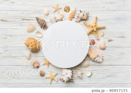 Summer time concept with blank greeting card and blank white paper on colored background. Seashells from ocean shore in the shape of frame separated with space for text top view Summer time concept with blank greeting card and blank white paper on colored background. Seashells from ocean shore in the shape of frame separated with space for text top view 90957155