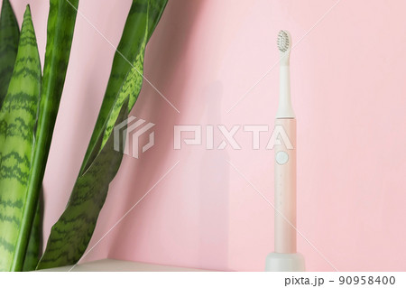 New modern ultrasonic toothbrushes. Dental care supplies with green leaves on pink pastel background. Oral hygiene, gum health, healthy teeth. Dental products Ultrasonic vibration toothbrush. New modern ultrasonic toothbrushes. Dental care supplies with green leaves on pink pastel background. Oral hygiene, gum health, healthy teeth. Dental products Ultrasonic vibration toothbrush. 90958400