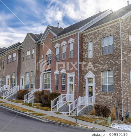 Square frame Townhouses with stairs at entrance against snowy mountain and cloudy blue sky 90959156