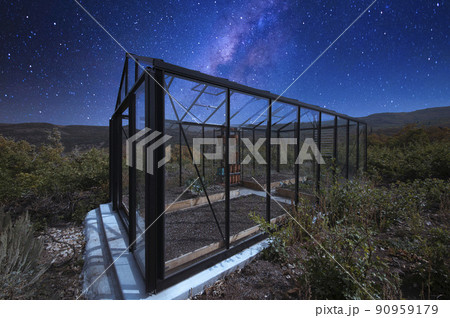 Glass greenhouse in the middle of a shrubland under the starry composite milky way sky 90959179