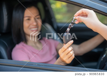 an attractive woman in a car gets the car keys. rent or purchase of auto - concept. professional salesperson during work with customer at car dealership. giving keys to new car owner. 90965830
