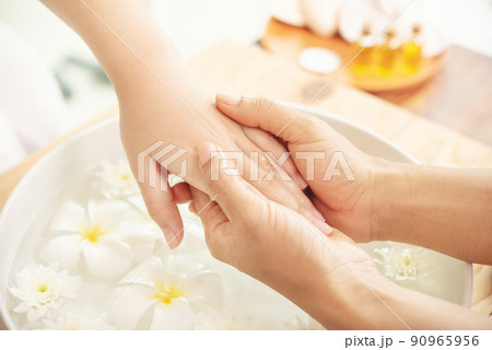 Beautician massaging hand of female spa salon client. Spa treatment and product for female feet and hand spa. white flowers in ceramic bowl with water for aromatherapy at spa. Beautician massaging hand of female spa salon client. Spa treatment and product for female feet and hand spa. white flowers in ceramic bowl with water for aromatherapy at spa. 90965956