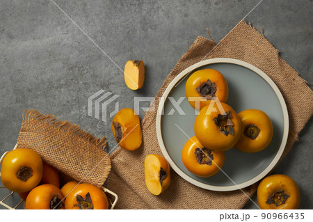 Top view of a grey dish of persimmon , brown paper in grey background for food advertising  90966435