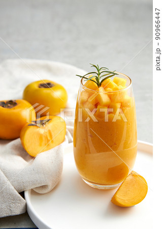 Front view of persimmon in white plate , green leaf , white napkin with grey background for food advertising Front view of persimmon in white plate , green leaf , white napkin with grey background for food advertising 90966447
