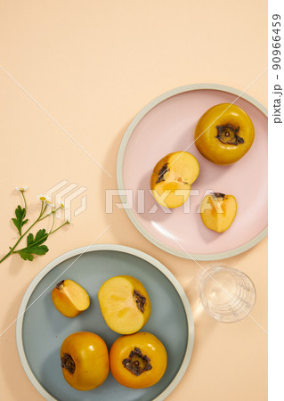 Top view of blue and pink dish of persimmon , pork , knife , water glass in light pink background for food advertising	 90966459