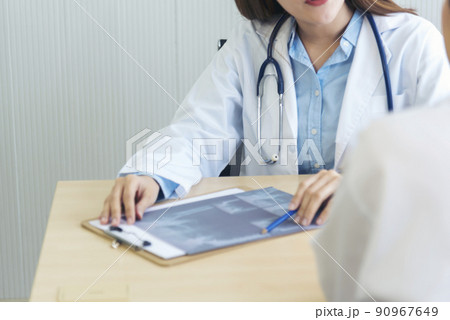Two asian women doctors discuss meeting doctor's office medical clinic looking x-ray film consulting patient disease. Asian medical lab young women talking together discussing healthcare teamwork Two asian women doctors discuss meeting doctor's office medical clinic looking x-ray film consulting patient disease. Asian medical lab young women talking together discussing healthcare teamwork 90967649