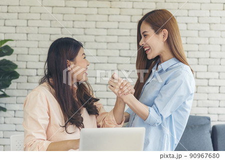 Asian colleague friendship at work with smiling face. Happiness two women colleague working together team meeting in office desk. Team business partners working with computer laptop startup company Asian colleague friendship at work with smiling face. Happiness two women colleague working together team meeting in office desk. Team business partners working with computer laptop startup company 90967680