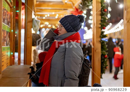 caucasian woman wearing hat and red scarf going to buy treats in kiosk at christmas market caucasian woman wearing hat and red scarf going to buy treats in kiosk at christmas market 90968229
