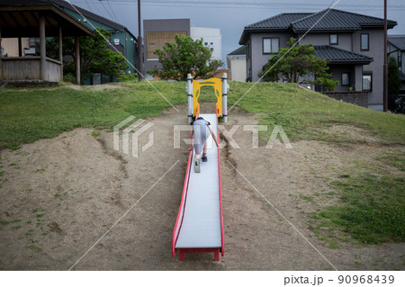 住宅地の公園で滑り台を遊んでいる小学生の女の子の様子 90968439