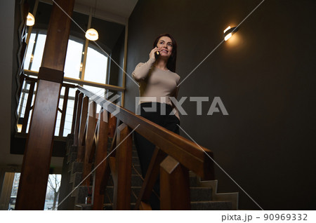 Confident successful elegant European business woman going down the stairs and talking on mobile phone. 90969332