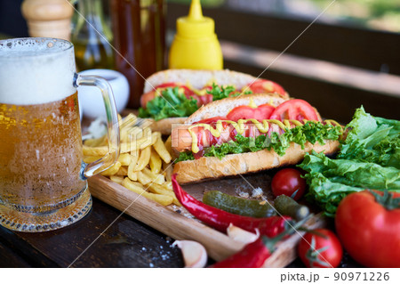 BBQ hot dog served with vegetables and French fries and sauces on wooden serving board BBQ hot dog served with vegetables and French fries and sauces on wooden serving board 90971226