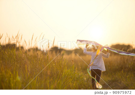 A girl runs into a field with a kite, learns to launch it. Outdoor entertainment in summer, nature and fresh air. Childhood, freedom and carelessness. A child with wings is a dream and a hope. 90975972