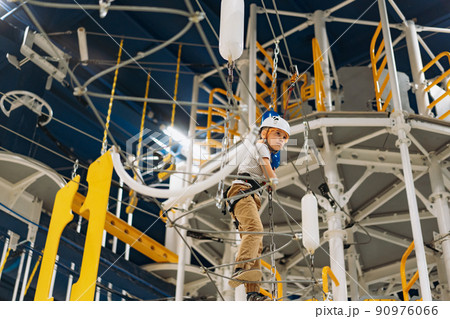 cute little boy climbing in adventure park passing obstacle course. high rope park indoors cute little boy climbing in adventure park passing obstacle course. high rope park indoors 90976066