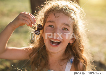 A cheerful sweet girl with cherry berries in her mouth. Funny summer portrait of a child with a cherry, gifts of summer, summer time. A cheerful sweet girl with cherry berries in her mouth. Funny summer portrait of a child with a cherry, gifts of summer, summer time. 90976270
