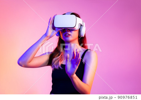 Metaverse concept young asian woman in black tank top wearing white vr headset hand touching watching and playing on the pink screen background.. 90976851