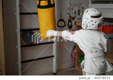 little boy in kimono and helmet training at home punching a punchbag 90978054