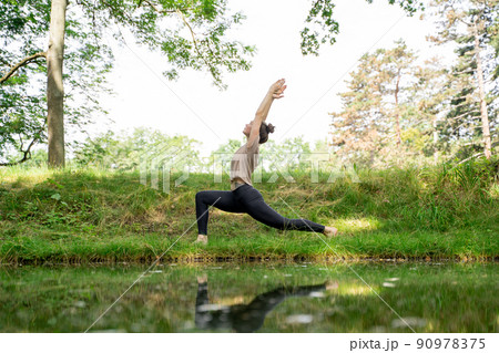Young woman doing sun salutation yoga practice on green grass loan in sunny park Young woman doing sun salutation yoga practice on green grass loan in sunny park 90978375