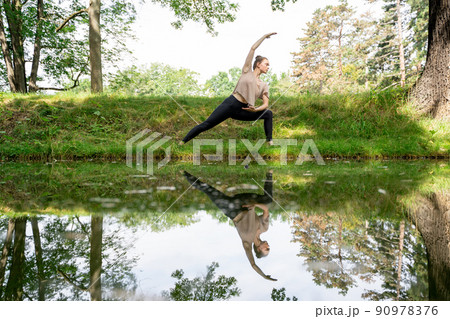 Young woman practicing yoga, pilates or stretching on grass near river in park 90978376