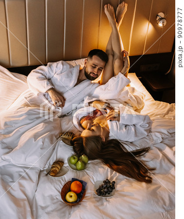 Happy young couple sitting in bed in morning and having breakfast Happy young couple sitting in bed in morning and having breakfast 90978777