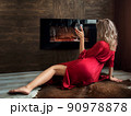 Woman sitting by fireplace with glass of wine 90978878
