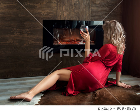 Woman sitting by fireplace with glass of wine Woman sitting by fireplace with glass of wine 90978878