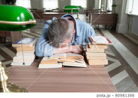 Senior man falls asleep over a textbook, he is sitting at a table Senior man falls asleep over a textbook, he is sitting at a table 90981366