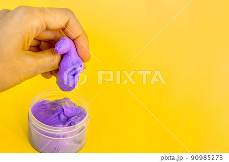 A woman's hand crumples purple rubber taken out of a jar on a bright yellow background. Anti-stress toy for stress relief and rehabilitation therapy of hand injuries. Copy space A woman's hand crumples purple rubber taken out of a jar on a bright yellow background. Anti-stress toy for stress relief and rehabilitation therapy of hand injuries. Copy space 90985273