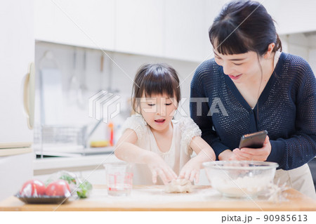 ママとスマホでレシピを見ながら料理をする娘 90985613
