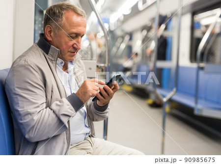 Elderly passenger is engrossed in information on smartphone while traveling in subway car 90985675