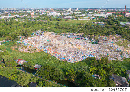 Aerial view of stack of different types of large garbage pile, plastic bags, and trash with a tractor car in industrial factory in environmental pollution. Waste disposal in dumping site. 90985707