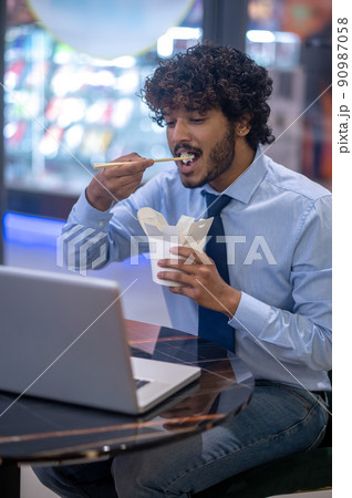 Man eating looking at laptop screen 90987058