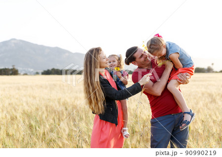 Happy family father of mother and two daughters sisters on nature at sunset.Carefree parents having fun with their kids on a field. Happy family father of mother and two daughters sisters on nature at sunset.Carefree parents having fun with their kids on a field. 90990219