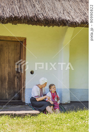 mother and daughter are sitting near the house in Ukrainian folk dresses mother and daughter are sitting near the house in Ukrainian folk dresses 90990822