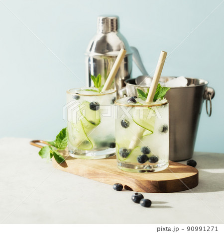 Trendy summer drinks with cucumber, mint and blueberry on blue sky background Trendy summer drinks with cucumber, mint and blueberry on blue sky background 90991271