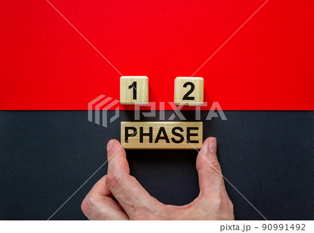 Businessman holds a block with word 'phase'. Wooden cubes with numbers 1 and 2. Beautiful red and black background. Copy space. Concept of choice. Businessman holds a block with word 'phase'. Wooden cubes with numbers 1 and 2. Beautiful red and black background. Copy space. Concept of choice. 90991492
