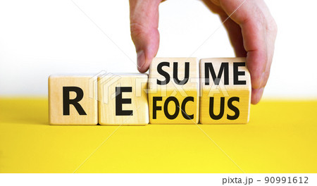 Refocus and resume symbol. Businessman turns cubes and changes the word 'refocus' to 'resume'. Beautiful yellow table, white background. Business refocus and resume concept. Copy space. 90991612