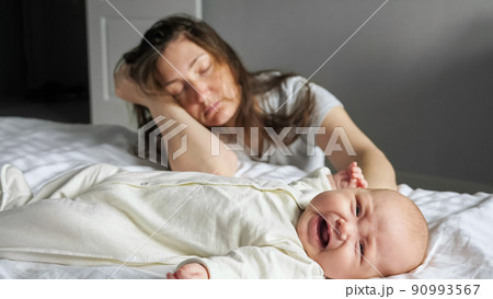 Tired mother sleeps sitting on floor near crying baby girl Tired mother sleeps sitting on floor near crying baby girl 90993567