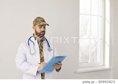 Portrait of military doctor in camouflage uniform and medical lab coat with clipboard 90993823